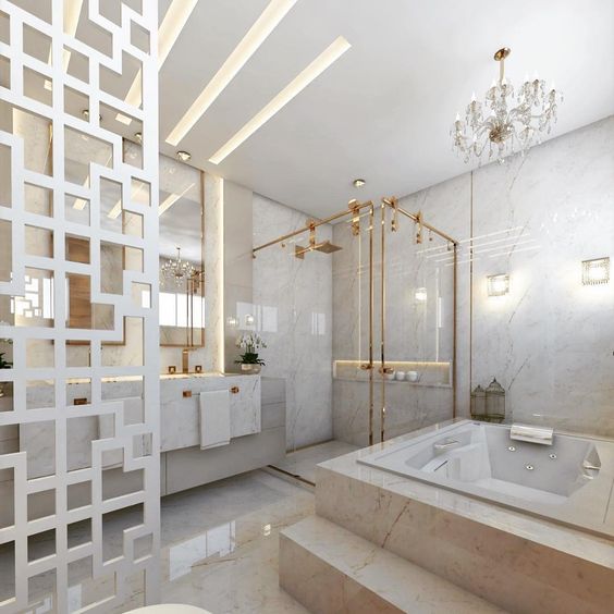 Banheiro planejado grande e luxuoso. Todo em mármore e metais dourados. A banheira é grande e o ambiente iluminado. 