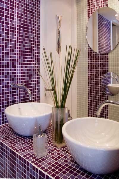 Banheiro com duas pias, vaso de planta e paredes de pastilha roxa e branca.