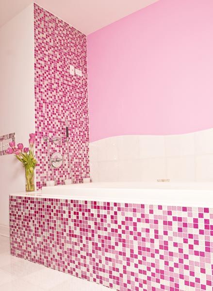 Banheiro decorado com banheira, vaso de flores e pastilha rosa e roxa.