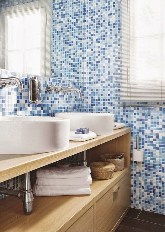 Banheiro com armário de madeira, cubas brancas e paredes de pastilha azul.