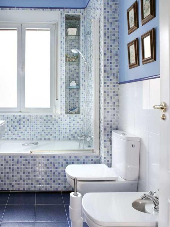 Banheiro com paredes divididas em branco e azul e decoradas com quadros.