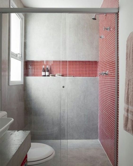 Banheiro cinza acimentado com parede vermelha de pastilha.