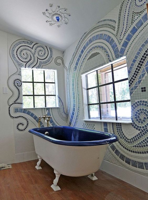 Banheiro com banheira branca e azul e paredes desenhadas com pastilha.