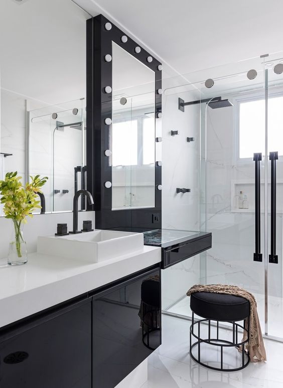 Banheiro branco com armário, banco e moldura do espelho pretos.