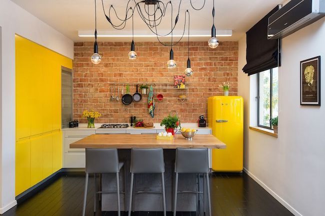 Cozinha decorada com papel de parede de tijolinhos aparentes e armários amarelos.