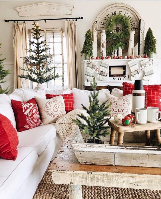 Decoração de natal para sala simples com árvores pequenas, guirlandas discretas e almofadas vermelhas.