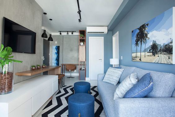 Sala de estar pequena com parede, quadros e almofadas azuis.