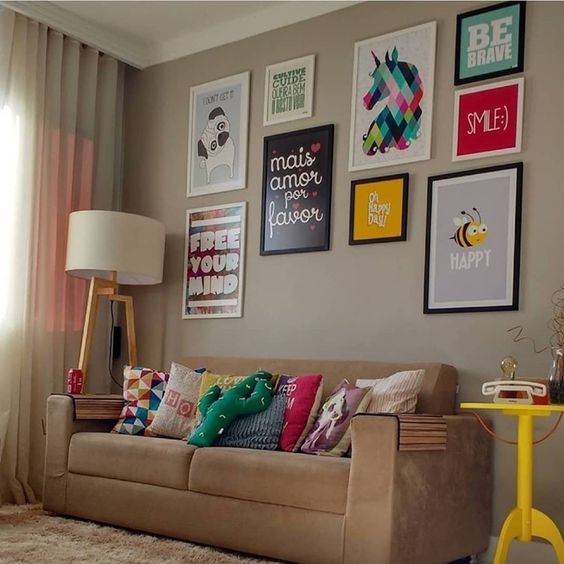 Sala com sofá bege e muitos quadros e almofadas coloridas.