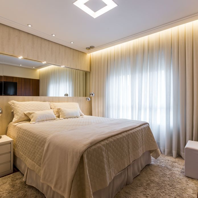 Quarto de casal com iluminação embutida no teto e luminárias suspensas ao lado da cama.